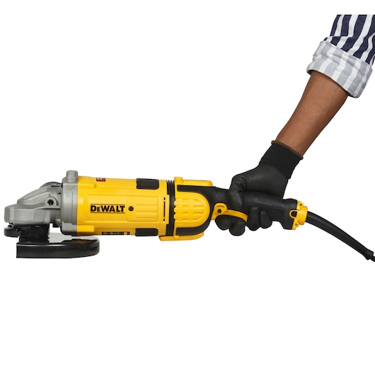 A person wearing a black glove and striped sleeve is holding a yellow DEWALT angle grinder with a black power cord against a white background.
