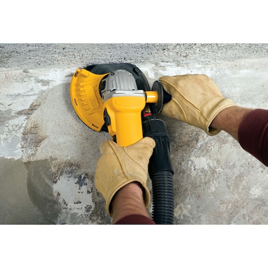 Close-up of gloved hands operating a yellow DEWALT power tool, grinding and smoothing a concrete surface.