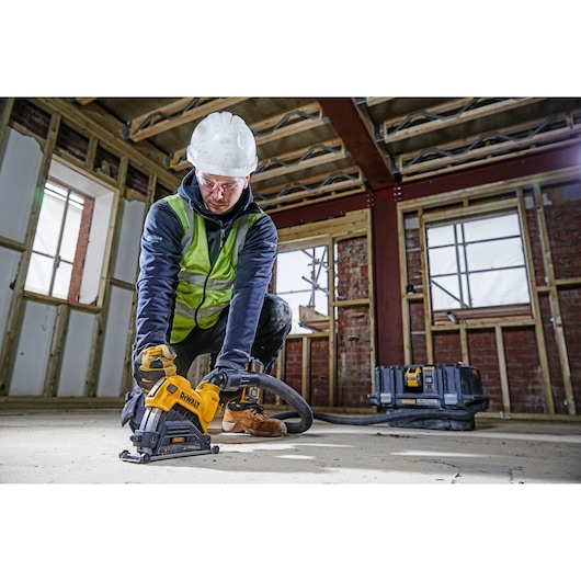 Worker using DEWALT DWE46225 saw at a construction site, wearing safety gear and cutting concrete floor.