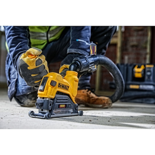 Worker uses DEWALT DWE46225 power tool with dust extractor on concrete floor at a construction site.