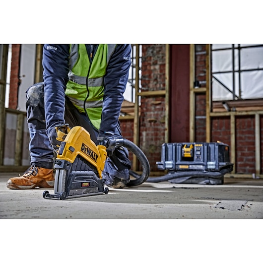 Person using DEWALT wall chaser tool on concrete floor at construction site. Tool case visible in background.