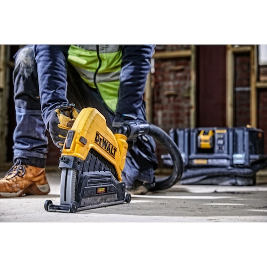 Worker using a DEWALT power tool on the floor; tool case and hose are visible in the background.