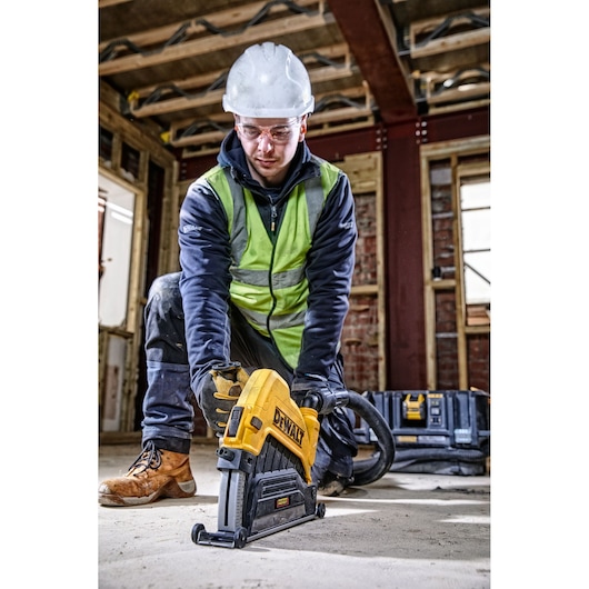 Worker uses DEWALT power tool on construction site floor, wearing safety gear and handling tool with gloves.