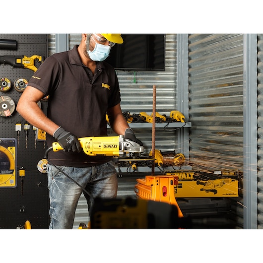 Person using a DEWALT DWE492 angle grinder to cut metal, with sparks in a workshop setting.
