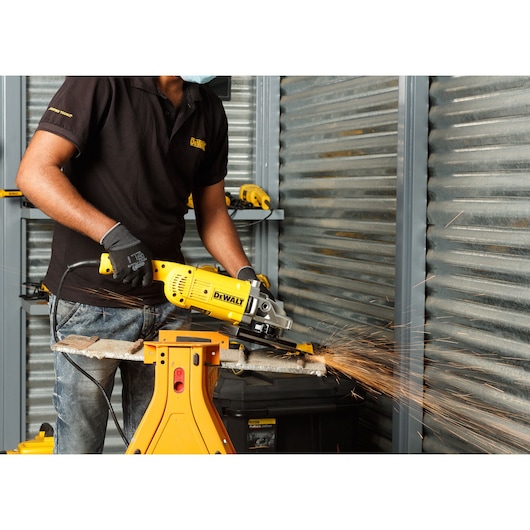 Person using a DEWALT DWE492 grinder on metal, producing sparks in a workshop with safety gloves.