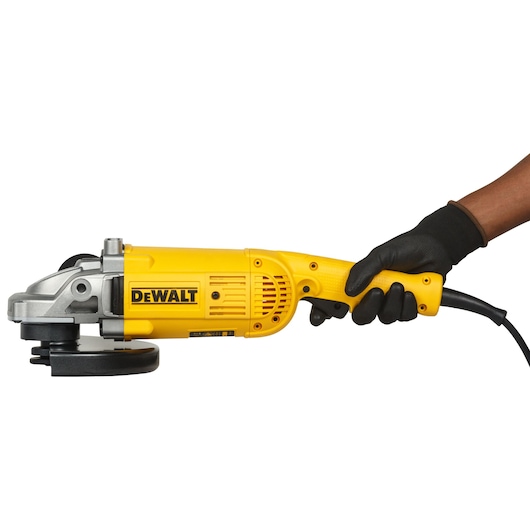 A person wearing a black glove is holding a yellow DEWALT DWE492 angle grinder with a cord, shown against a white background.