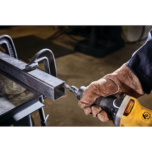 Gloved hand using a DEWALT tool to grind metal inside a square tube held by clamps on a workbench.