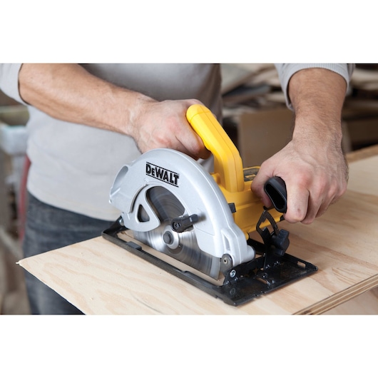 A person using a DEWALT DWE560 circular saw to cut a piece of wood. The tool features a yellow handle and a silver blade housing.