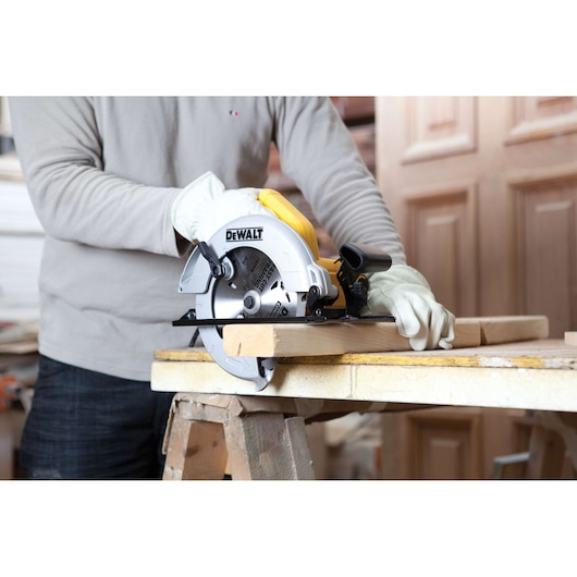 A person wearing gloves is using a DEWALT circular saw (model DWE560) to cut a wooden plank on a workbench.