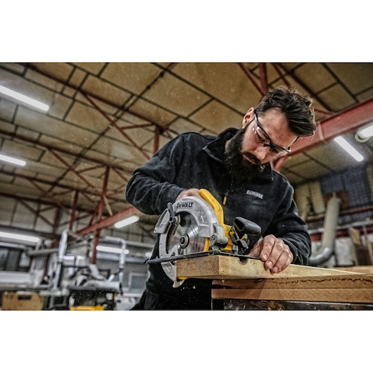 Person using a DEWALT DWE560 circular saw to cut wood in a workshop. Face is blurred for privacy.