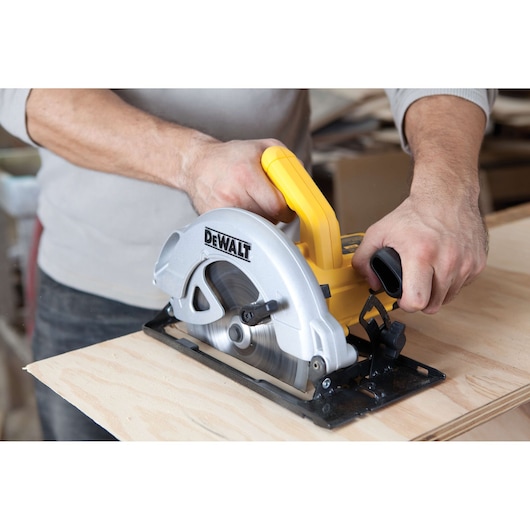 A person using a DEWALT DWE560 circular saw to cut a piece of wood. The tool features a yellow handle and a silver blade housing.