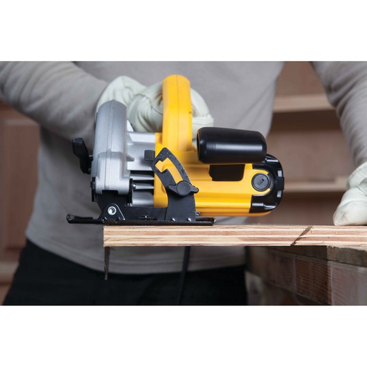 A person wearing gloves is using a yellow and black DEWALT circular saw to cut a piece of wood.