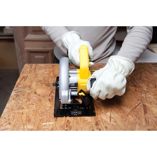 Person wearing white gloves operating a DEWALT circular saw on a wooden surface.