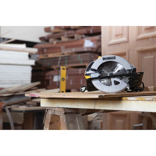 A DEWALT DWE560 circular saw placed on a wooden workbench in a workshop with stacks of wood in the background.