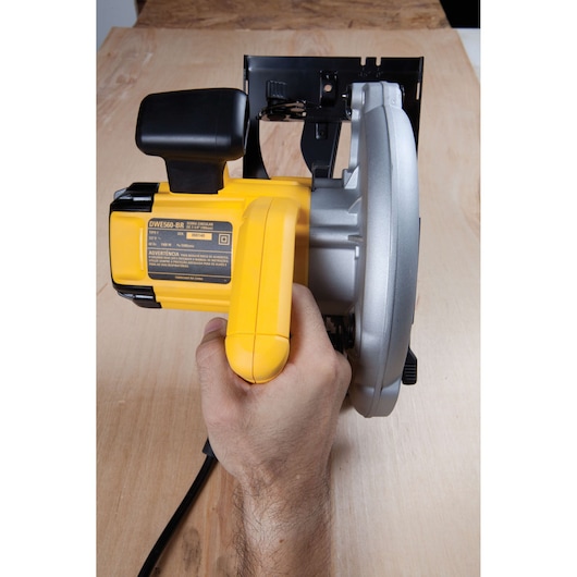 Hand holding a DEWALT DWE560 circular saw above a wooden surface.