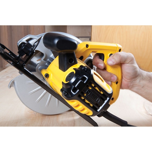Close-up of a hand holding a yellow DEWALT circular saw cutting wood.