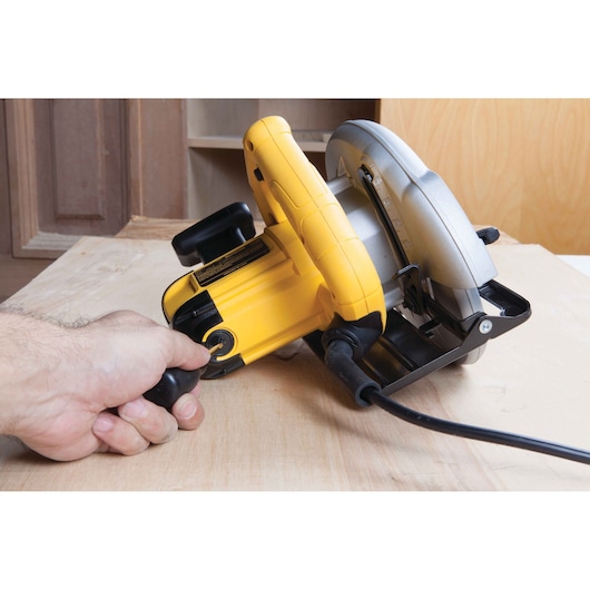Hand holds a yellow DEWALT DWE560 circular saw cutting wood in a workshop.