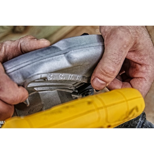 Close-up of a person adjusting the angle setting on a DEWALT circular saw, focusing on the adjustment mechanism and engraved measurement marks.