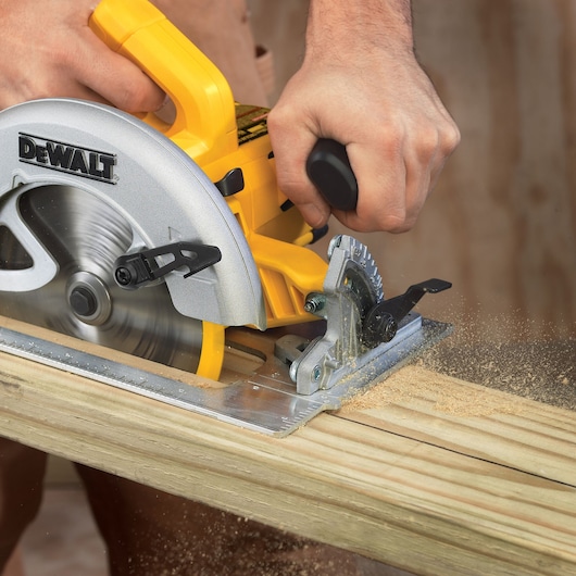 Person using a DEWALT circular saw to cut wood, sawdust flying as the blade moves through the plank.