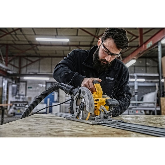 DEWALT circular saw in use on wood in a workshop, operator's face blurred for privacy.