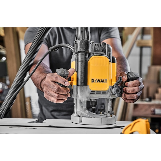 Hands operate a DEWALT router tool on a workbench in a woodworking workshop.