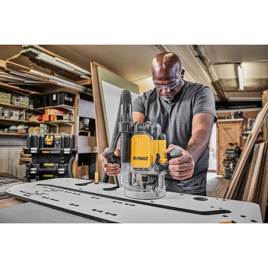 Person using a DEWALT DWE625KT router tool on a workbench in a workshop setting.