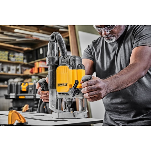 Person using a DEWALT router tool on a workbench in a workshop setting.