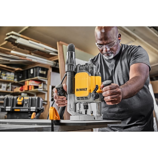 Person using DEWALT DWE625KT plunge router tool on a workbench in a workshop setting.