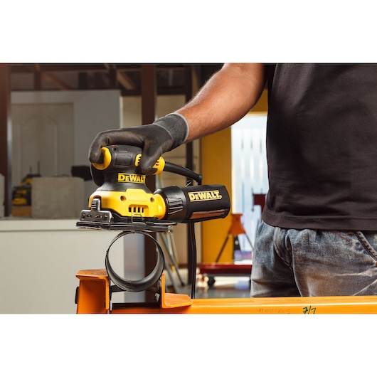 Hands connecting a hose to a yellow DEWALT power tool, used for woodworking or sanding.
