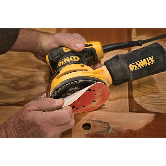 A person applies a sanding disc to a DEWALT electric sander, preparing it for use on a wooden surface.