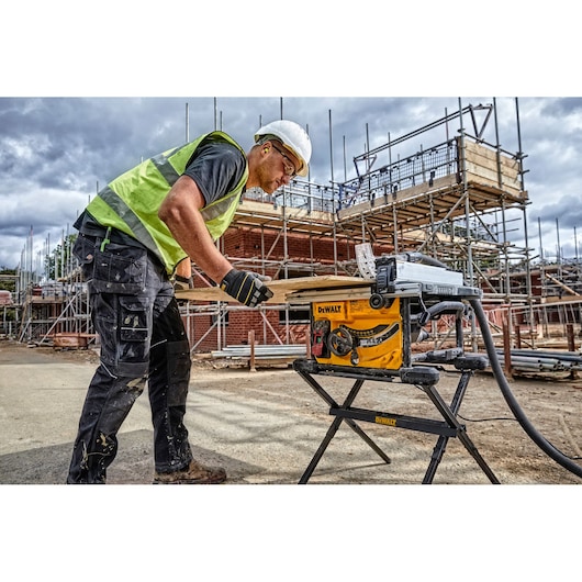DEWALT DWE7485WS and DWE7485 saw used outdoors at construction site. Worker cuts wood. Scaffolding in background.