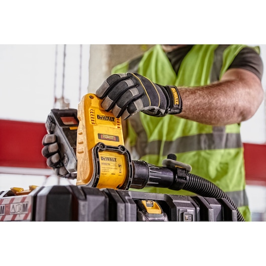 Person wearing gloves operates DEWALT DWH079D tool near a toolbox, hose attached. High-visibility vest visible.