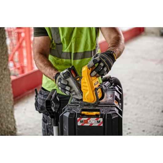 Worker in gloves handling a DEWALT tool with a battery on a jobsite toolbox.