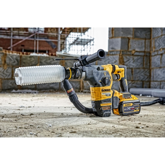 DEWALT cordless hammer drill with dust extractor attachment on a construction site floor with brick wall in background.