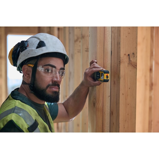 Worker uses DEWALT laser distance measurer on wooden beam at construction site.