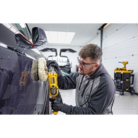 Person using a DEWALT DWP849X polisher on a car in a garage setting. Tool cart visible in background.