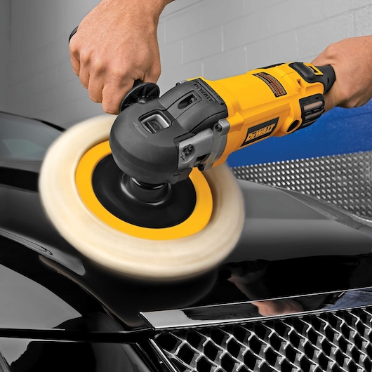 A DEWALT polisher is being used to polish a black car hood, held by a person’s hands.