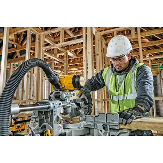 Worker using a DEWALT DWS727 saw at a construction site, wearing safety gear and gloves.