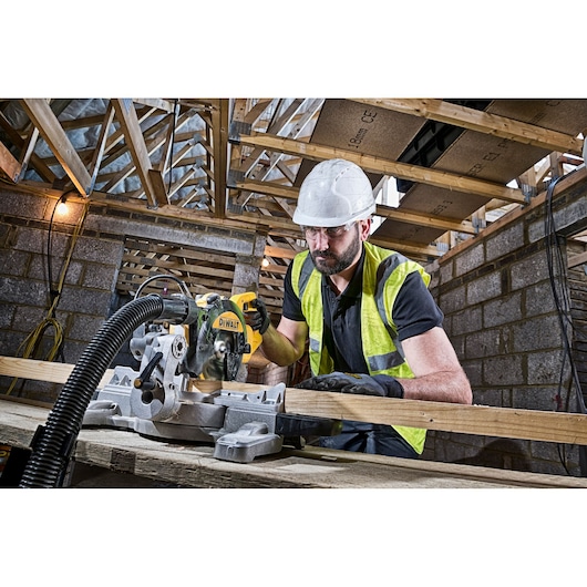 Worker uses DEWALT DWS774 saw to cut wood in a construction site, wearing a hard hat and safety vest.