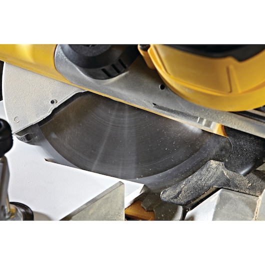 Close-up of a DEWALT mitre saw blade cutting wood, showing detail and dust during operation.