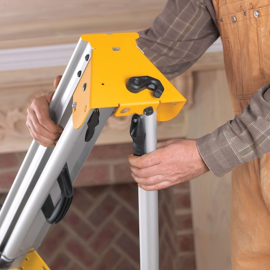 Close-up of a person adjusting a DEWALT miter saw stand, showing hands securing the legs of the yellow and silver stand.