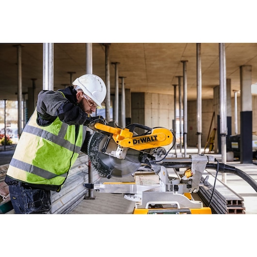 DEWALT DWS780, DWS780KIT saw in use at a construction site. Worker wears safety gear. Photography product category.