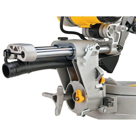 Close-up view of a DEWALT DWS780 miter saw, focusing on the sliding mechanism and dust collection port. The saw features metallic and yellow parts with adjustment levers and a sturdy construction.