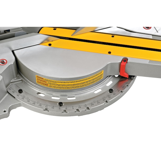 Close-up view of the DEWALT DWS780 miter saw base, showing the angle scale, adjustment knob, yellow fence, and safety warning label.