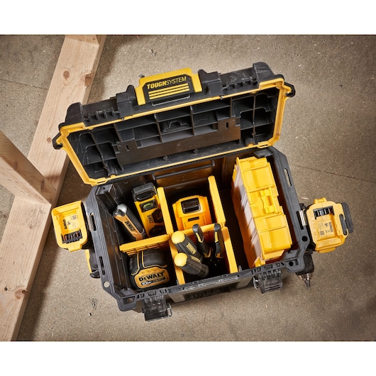 Open DEWALT ToughSystem toolbox containing various yellow and black tools and accessories, placed on a concrete floor next to wooden beams.