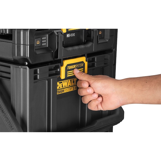 A close-up of a hand engaging the yellow latch of a DEWALT TOUGHSYSTEM 2.0 black modular storage box.