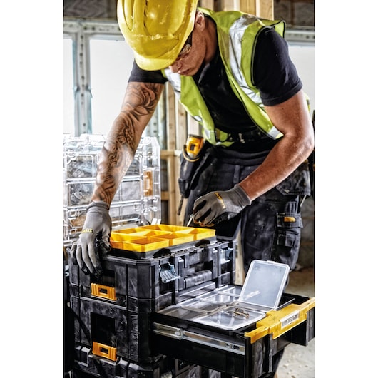 Worker using DEWALT DWST1-70705 tool organizer with yellow compartments at a construction site.