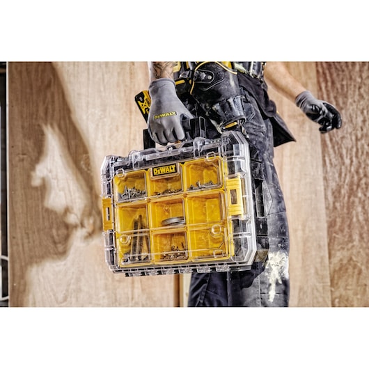 Person holding a DEWALT yellow transparent organizer box with compartments, filled with screws and small parts.