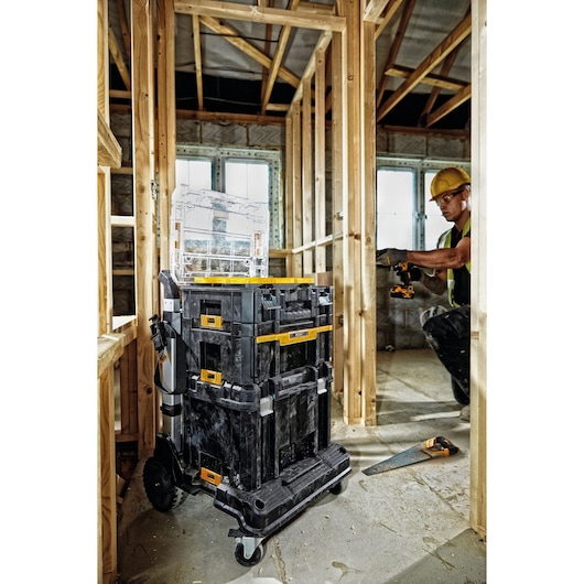 DEWALT tool storage trolley in a construction area with worker using power tool in background.