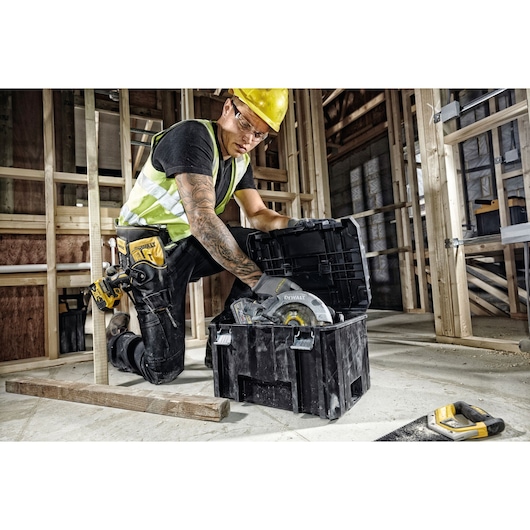 DEWALT toolbox DWST1-71195 with circular saw in use on a construction site, worker kneeling and opening lid.
